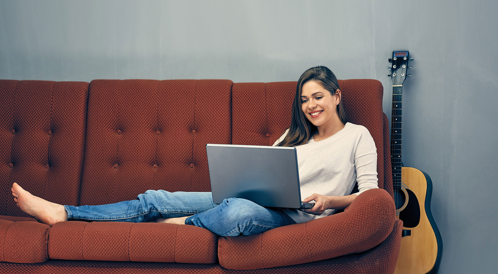 En kvinna som ligger i en soffa med en bärbar dator.